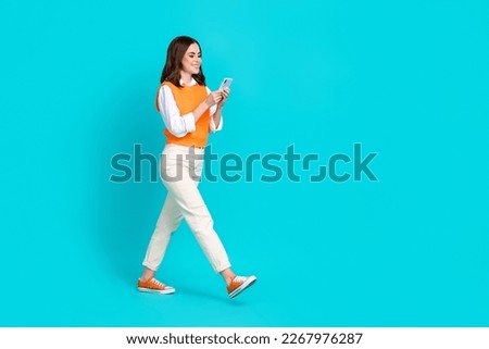 Full length size photo of positive satisfied lady wear stylish vest with pants hold phone remote chat isolated on aquamarine color background