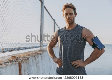 Young strong sporty athletic toned fit sportsman man 20s in sports clothes warm up training mobile cell phone stand akimbo at sunrise sun over sea beach outdoor on pier seaside in summer day morning. Royalty-Free Stock Photo #2268003133