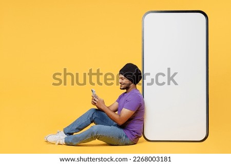Full body devotee Sikh Indian man ties his traditional turban dastar wear purple t-shirt sit big huge blank screen mobile cell phone use smartohone isolated on plain yellow background studio portrait Royalty-Free Stock Photo #2268003181