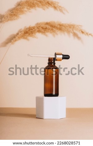 Brown cosmetic serum bottle on a podium and pampas grass on beige background. Natural skin care cosmetics concept. Closeup.