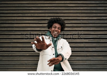 Happy funky gen z hipster rapper African American guy dancing, singing, having fun feeling hip-hop or rap vibe, moving and gesturing standing at wooden wall background outdoors. Royalty-Free Stock Photo #2268036145