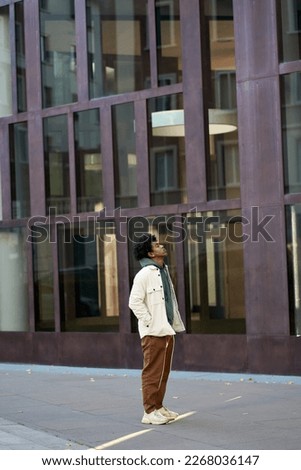 Confident cool young African American guy model standing big city at modern street buildings. Stylish ethnic rebel hipster gen z teen boy outdoors, breathing air with eyes closed, vertical. Royalty-Free Stock Photo #2268036147