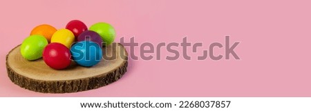 Wide Easter banner. Multi-colored eggs lie on a wooden boar, pink background. Holiday concept, congratulation, postcard, template,copy space, text, moc-up,handmade,spring,decoration,party,poster. Royalty-Free Stock Photo #2268037857