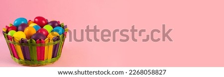 Wide Easter banner. Multi-colored eggs lie in a wicker basket, pink background. Holiday concept, congratulation, postcard, template,copy space, text, moc-up,handmade,spring,decoration,party,poster. Royalty-Free Stock Photo #2268058827