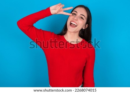 young woman wearing red shirt over white studio background Doing peace symbol with fingers over face, smiling cheerful showing victory