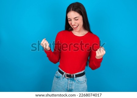 young brunette woman wearing red shirt over white studio background celebrating surprised and amazed for success with arms raised and eyes closed. Winner concept.