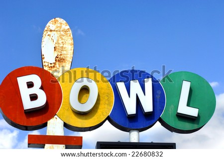 Old rusting sign says "BOWL".  Each letter is centered on a colored circle in red, yellow, blue and green.  Blue sky.