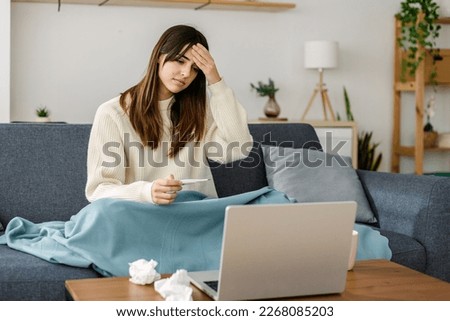 Young sick woman measuring fever touching forehead having a video call with doctor sitting on sofa in living room at home Royalty-Free Stock Photo #2268085203