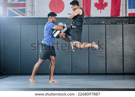 Healthy professional coach sparring and training male kickboxer indoors. Practice sports, exercise and fitness. Two muscular men fighting, jumping and blocking kicks with discipline in class. Royalty-Free Stock Photo #2268097887