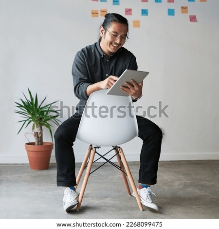Touching base with the business world. Full length shot of a handsome young businessman sitting on a chair and using his digital tablet at work.