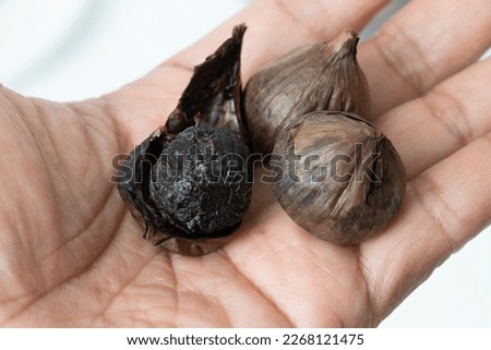 Closed up picture of  black garlic that not peeling and peeling lay on someone hand.