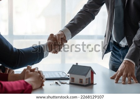 Two young Asian businessmen shake hands after signing a contract to invest in a village project. real estate, with businesswomen joining in showing joy and clapping in the office.