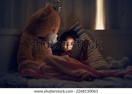 Watching her favourite cartoons before bed. Shot of a little girl using a digital tablet while lying in bed with her teddy at night.