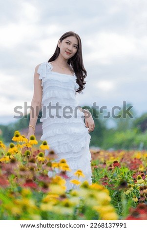 Beautiful Asian woman in garden with colorful flowers in foreground natural beauty while relaxing in park. Happy girl traveler with flower field sightseeing outfit vertical image