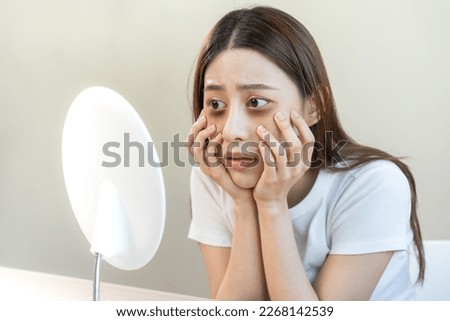 Bored, insomnia asian young woman, girl looking at mirror hand touching under eyes with problem of black circles or panda puffy, swollen and wrinkle on face. Sleepless, sleepy healthcare person.