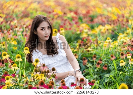Beautiful Asian woman in garden with colorful flowers in foreground natural beauty while relaxing in the garden. Happy girl with flower field dress, travel concept.