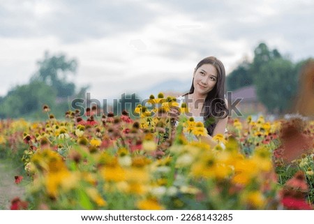 Beautiful Asian woman in garden with colorful flowers in foreground natural beauty while relaxing in the garden. Happy girl with flower field dress, travel concept.