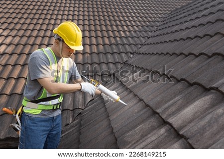 Worker man using silicone sealant adhesive  to fix crack of the old tile roof. Royalty-Free Stock Photo #2268149215