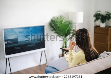 Asian woman Watching smart TV and using remote controller Hand holding television audio remote control at home with popcorn Royalty-Free Stock Photo #2268197381