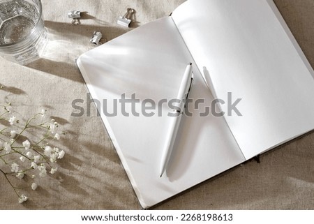 Open notebook blank sheets, pen and flowers on a neutral beige background with sunlight shadows, aesthetic home worckspace template. Flat lay, copy space