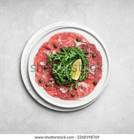 Beef carpaccio with capers, arugula and parmesan on a white plate, top view