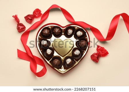 Heart shaped box with delicious chocolate candies and ribbon on beige background, flat lay