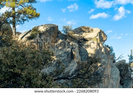 Rock formation on the side of cliff or ravine on mountain precipice for hikers to sit and for adventurers to rest upon in sun. Shade and blue sky with clouds in background and visible trees.