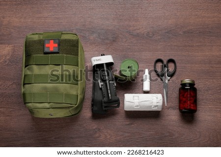 Flat lay composition with military first aid kit and tourniquet on wooden table