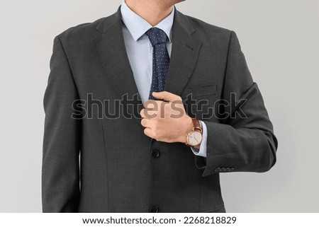 Stylish young businessman with watch on light background
