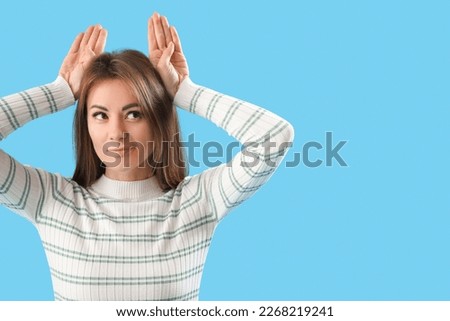 Beautiful woman making ears with her hands on blue background