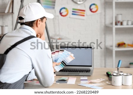 Male painter with color palettes and laptop on table in room