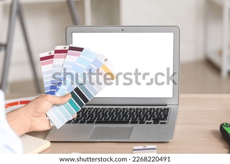 Male painter with color palettes and laptop on table in room, closeup