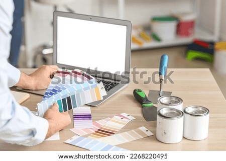 Male painter with color palettes using laptop at table in room, closeup