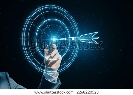 Target concept with a glowing hologram of bullseye and arrow hitting the center. Growth strategy. Goals achievement, success. Close up of businessman hand using hud screen on blurry dark background Royalty-Free Stock Photo #2268220523