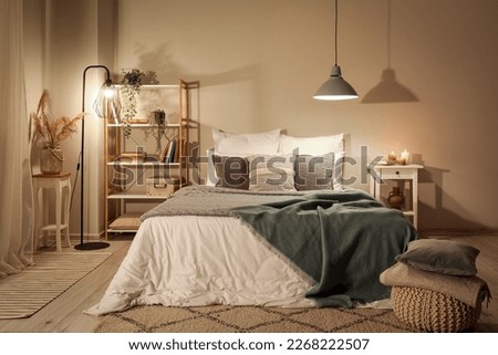 Interior of bedroom with green blankets on bed, burning candles and glowing lamps late in evening Royalty-Free Stock Photo #2268222507