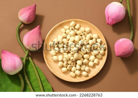 Top view of (Nelumbo nucifera) fresh lotus buds, green leaf and lotus seeds on wooden dish on brown background. Lotus flower is the Vietnamese national flower.