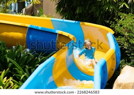 Kids on water slide in aqua park. Children having fun on water slides on family summer vacation in tropical resort. Amusement park with wet playground for young child and baby. Royalty-Free Stock Photo #2268246583