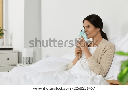 Young woman using nebulizer on bed at home, space for text Royalty-Free Stock Photo #2268251457