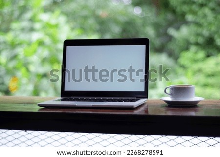 laptop with white screen and a coffee in white cup on the table garden view