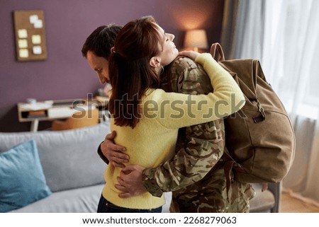 Side view portrait of young woman welcoming military man coming back home and embracing