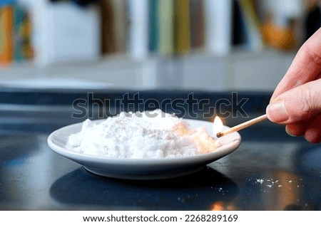 Hand ignites urotropin mixed with calcium gluconate, selective focus. Concept of chemistry lesson, chemical experiment Royalty-Free Stock Photo #2268289169