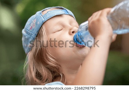 Drinking Water from Bottle. Thirsty Child Little Girl Baby Drink Water on Green Nature Background Outside. Royalty-Free Stock Photo #2268298795