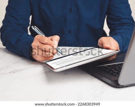 Signature electronic concept. A Businessman signing a digital contract or agreement on a tablet while sitting at the table in the office. Business and technology concept