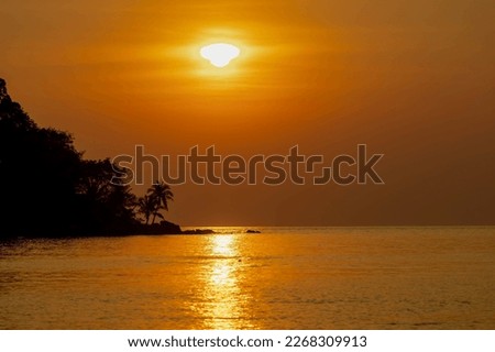 Silhouette of mountain, palm tree and rocks on seashore, Landscape view with warm golden skyline in the evening while the sun going down, Colourful sunset with orange sky in summer, Nature background.