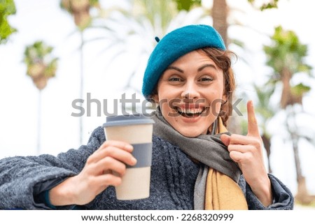 Brunette woman holding a take away coffee at outdoors pointing up a great idea