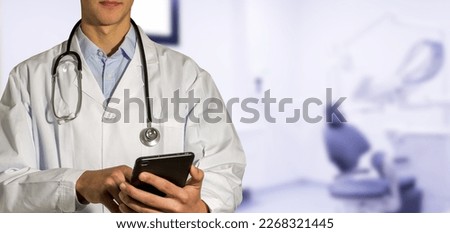 A doctor in a white coat holding a phone in his hand.