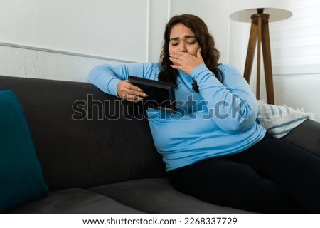 Depressed hispanic woman crying looking at a photo frame looking sad and heartbroken because of her breakup
