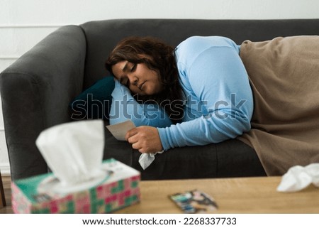 Heartbroken sad fat woman looking at a picture of her ex-boyfriend and missing him after breaking up while lying on the sofa