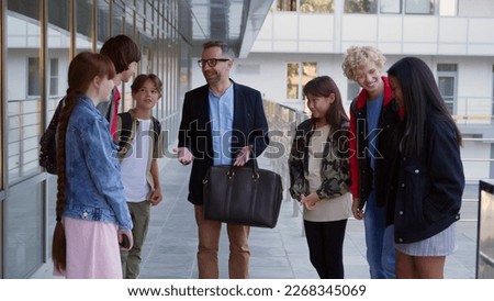 Happy diverse high school students talking to mature teacher outdoors. Smiling male professor communicate with group of multiethnic teen schoolkids outside school building. High quality photo