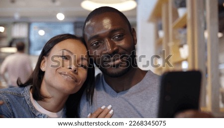 Happy couple taking selfie in cafe. Young attractive man holding camera and taking photo hugging smiling brunette woman on date in restaurant